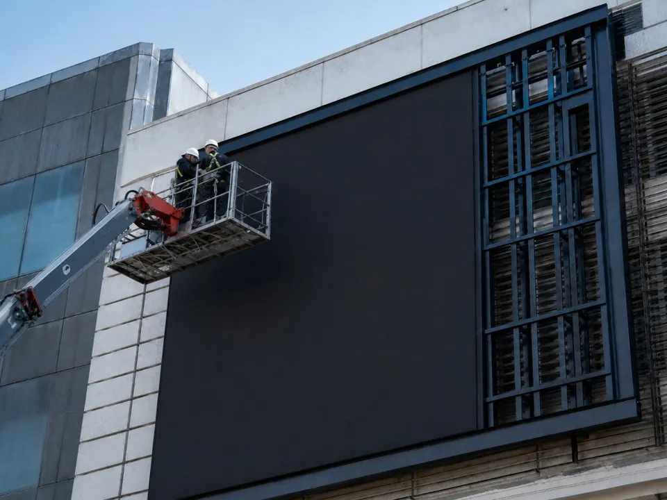 Installer on an aerial work platform fitting LED cabinets to a building facade